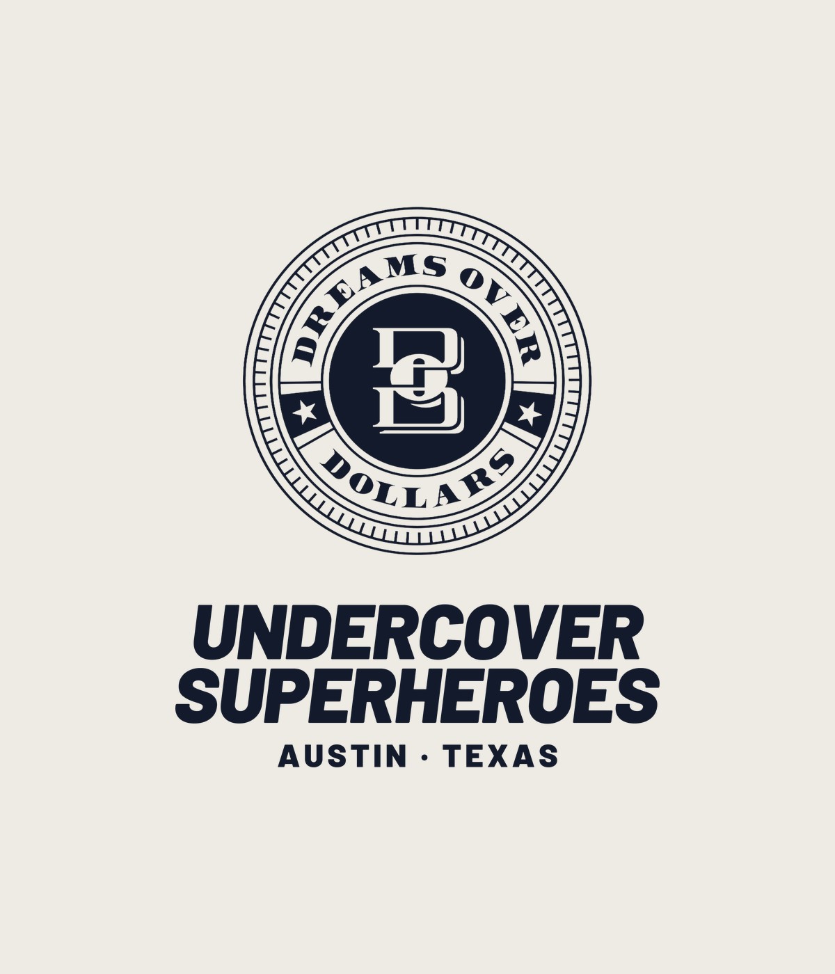 Cream t-shirt with the navy Dreams Over Dollars seal above Undercover Superheroes wordmark and Austin Texas